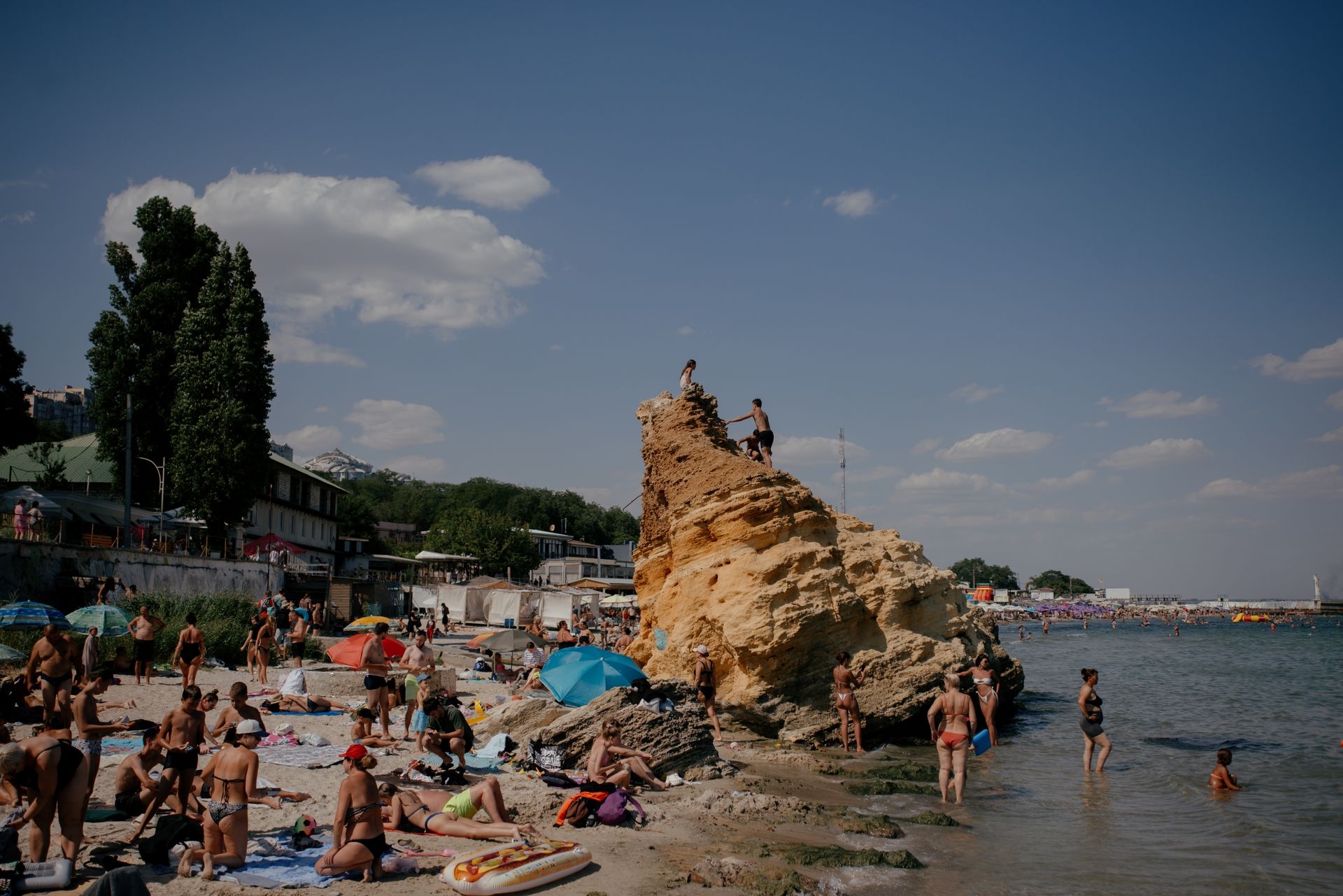 People relax on the beach as others climb a rock along the Black Sea coast in Odesa, Ukraine, on Aug. 9, 2025.