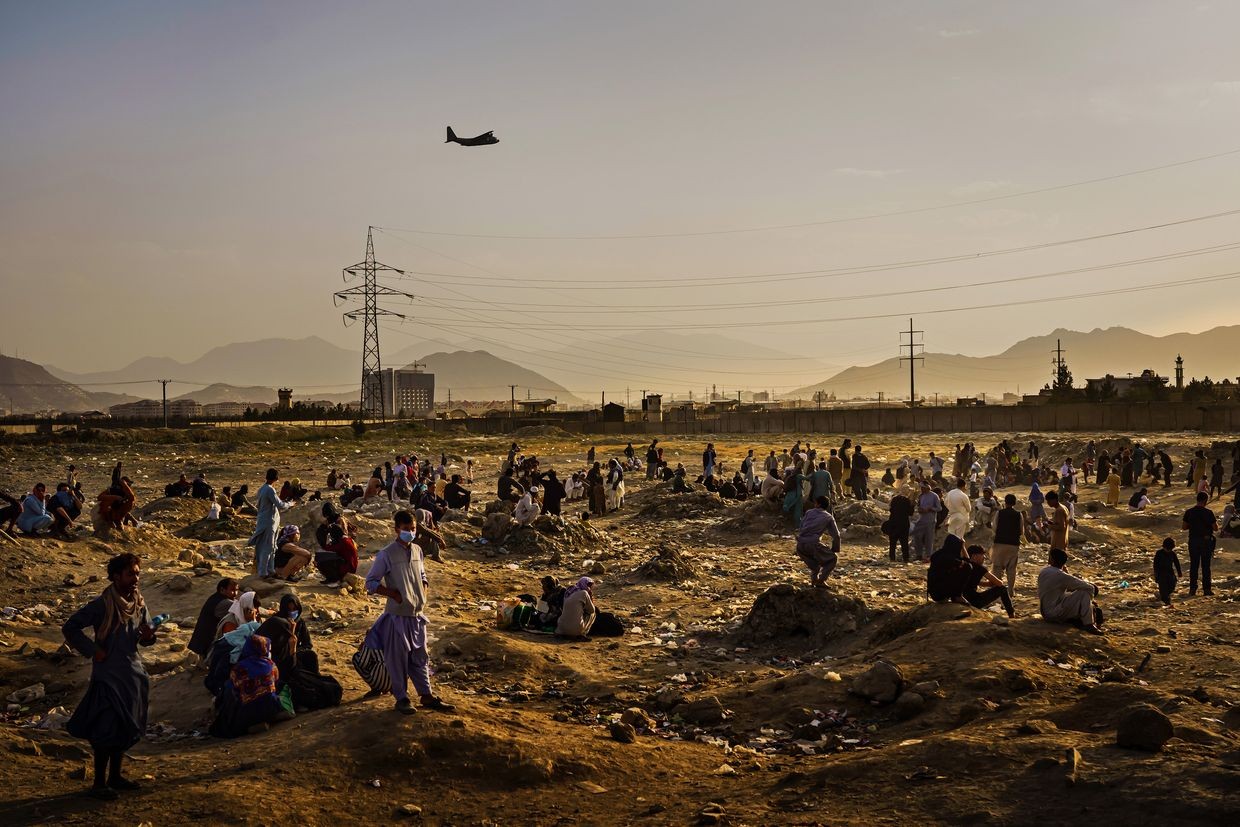 A military transport plane flies overhead as Afghans wait outside Kabul airport, Afghanistan on Aug. 23, 2021.