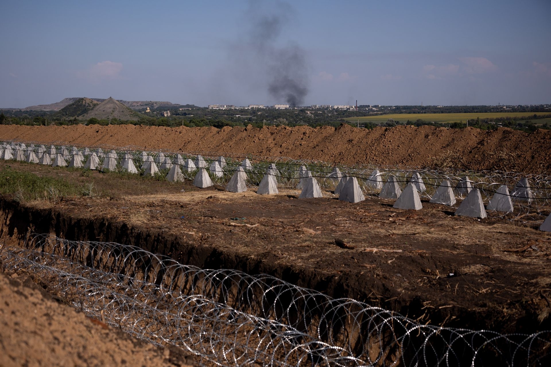 Fortifications, including dragon’s teeth and barbed wire, stand in front of smoke rising over Dobropillia after the detonation of an aerial bomb in Rodynske, Donetsk Oblast, Ukraine, on July 16, 2025.Fortifications, including dragon’s teeth and barbed wire, stand in front of smoke rising over Dobropillia after the detonation of an aerial bomb in Rodynske, Donetsk Oblast, Ukraine, on July 16, 2025.
